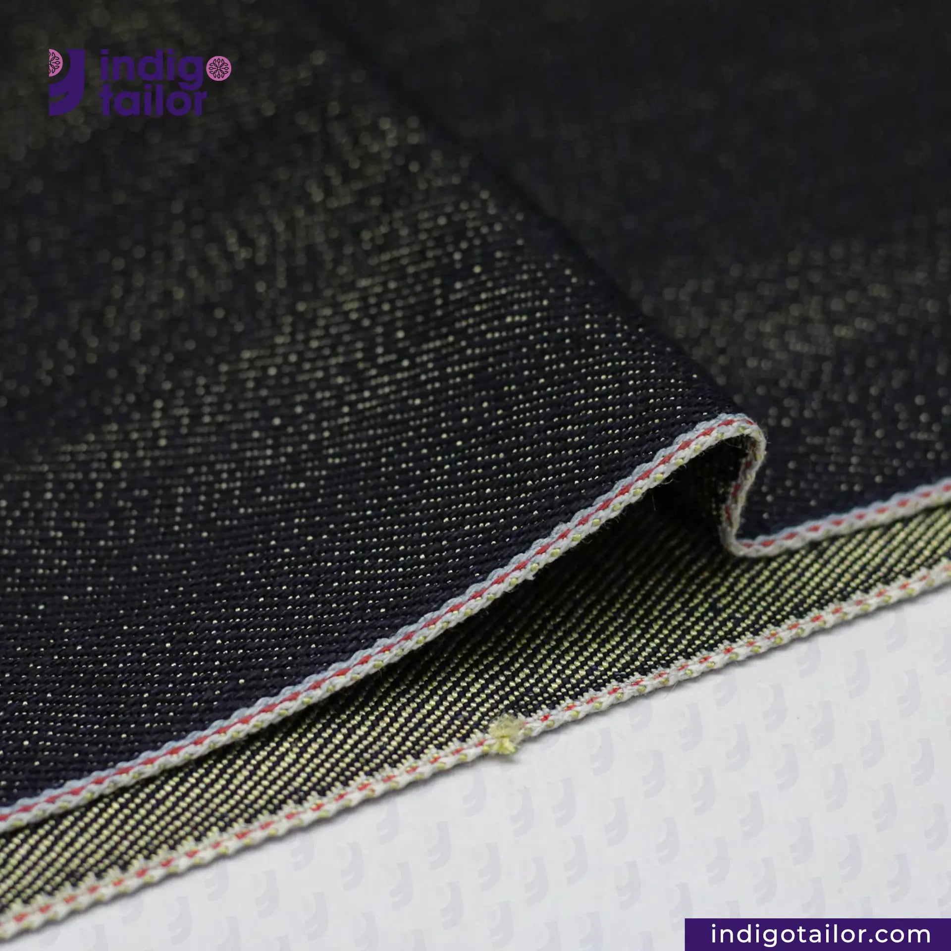 Close-up of black denim fabric with a visible brand logo on a white background. BULLION GOLD SELVEDGE DENIM