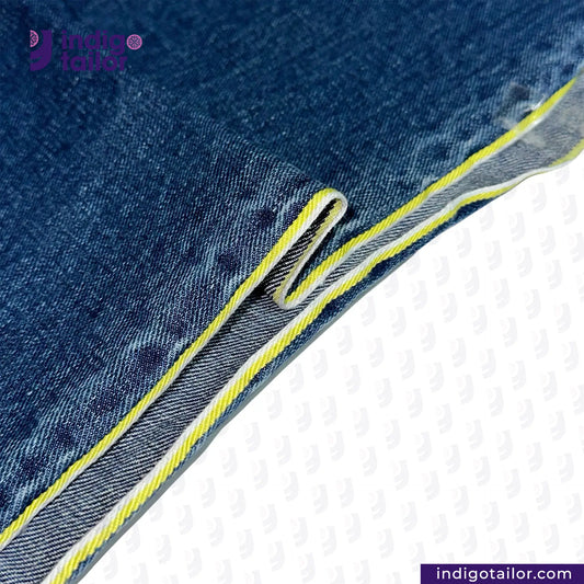 Close-up of DARK WASHED SELVEDGE DENIM LIME SELVEDGE ID fabric with yellow stitching on a white background, featuring the Indigo Tailor logo.