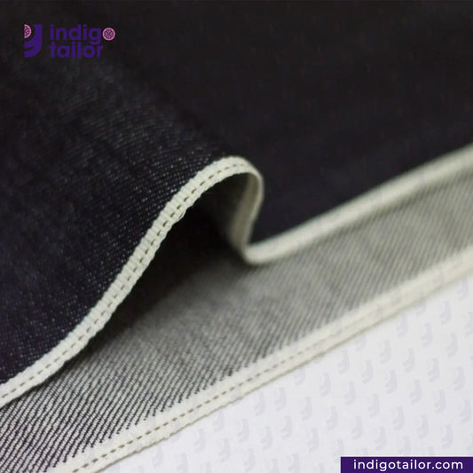 Close-up of DEEP INDIGO DOTTED BRONZE SELVEDGE fabric with 'Indigotailor' branding on a dark background