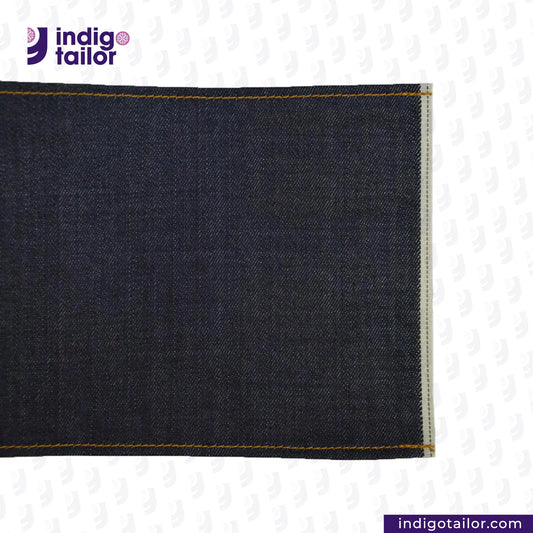 Close-up of DEEP INDIGO DOTTED BRONZE SELVEDGE fabric with 'Indigo Tailor' logo and website URL.