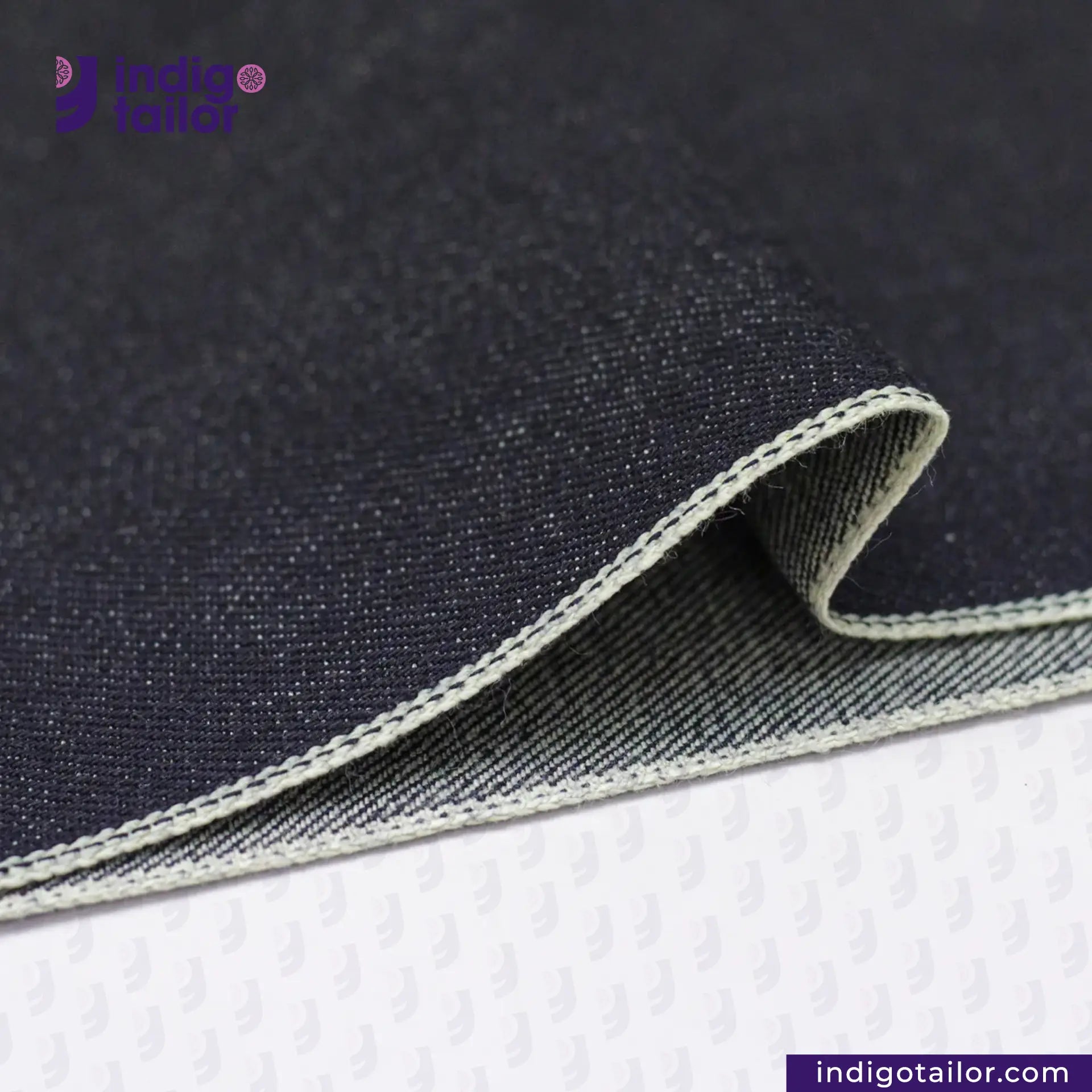 Close-up of DEEP INDIGO GREENCAST SELVEDGE DENIM fabric with a visible brand logo on a white background