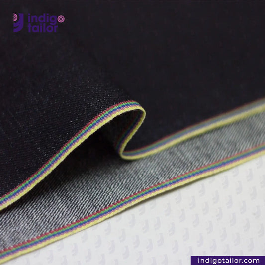 Close-up of DEEP INDIGO RAINBOW STRETCH SELVEDGE DENIM fabric with a colorful stripe on a textured surface, featuring the Indigotailor logo.