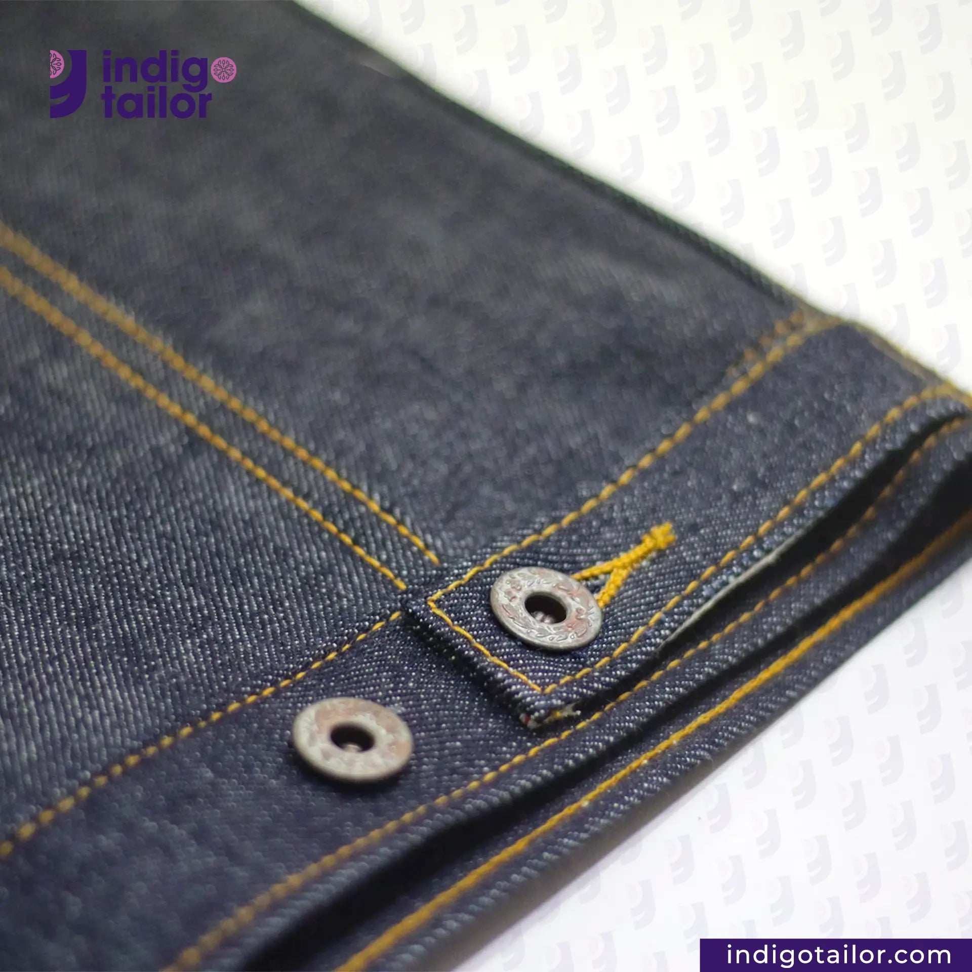 Close-up of DENIM BIKER VEST Cuff with yellow stitching and a button, branded 'Indigotailor'.