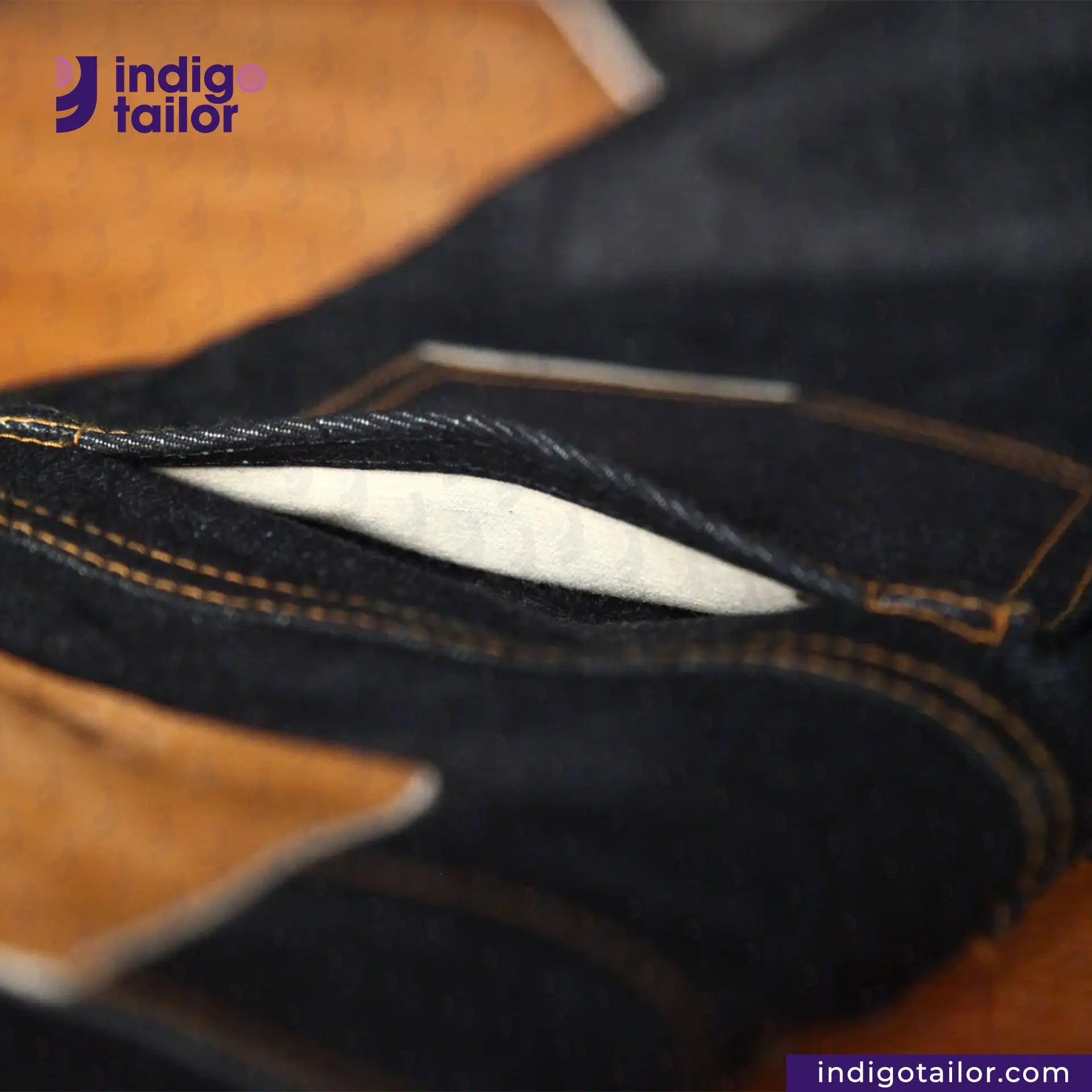 Close-up of dark denim fabric with 'indigotailor' branding.