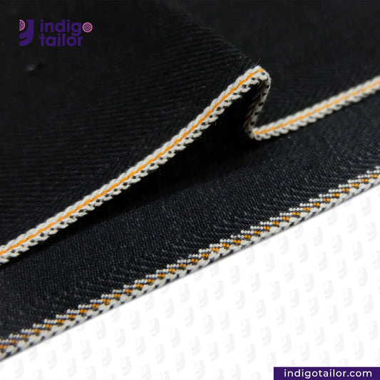 Close-up of HEAVY DOUBLE BLACK ORANGE SELVEDGE ID fabric with white and orange stitching, featuring the Indigotailor logo.