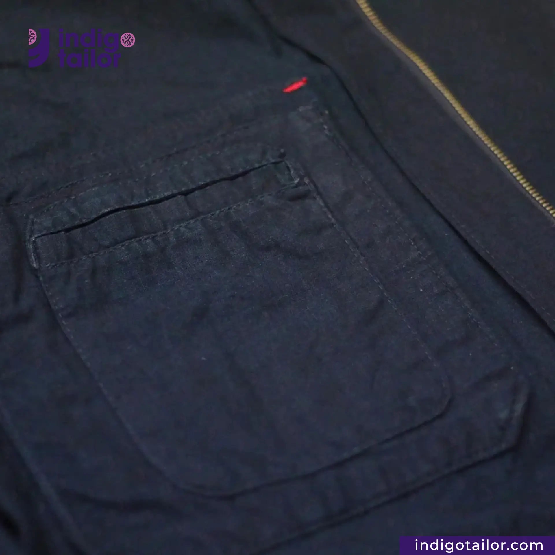 Close-up of a INDIGO HARRINGTON JACKET with a pocket and zipper, featuring the brand 'Indigo Tailor'.
