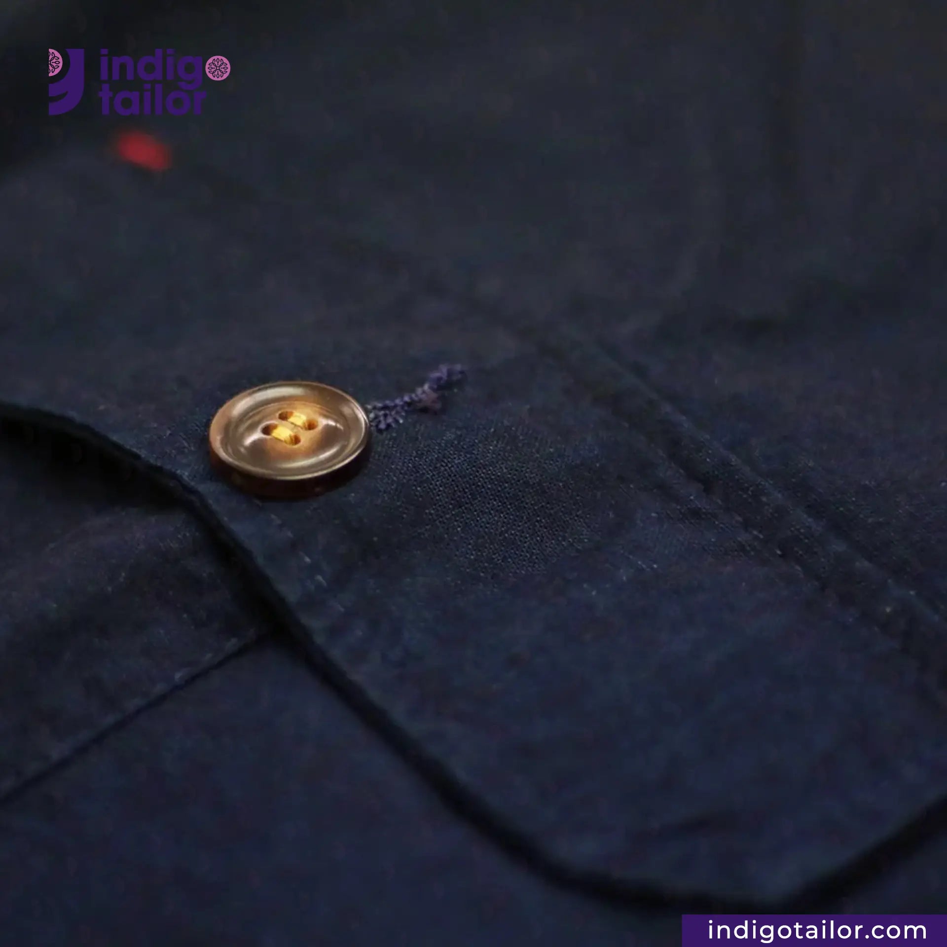 Close-up of a button on a INDIGO HARRINGTON JACKET with 'Indigotailor' branding.