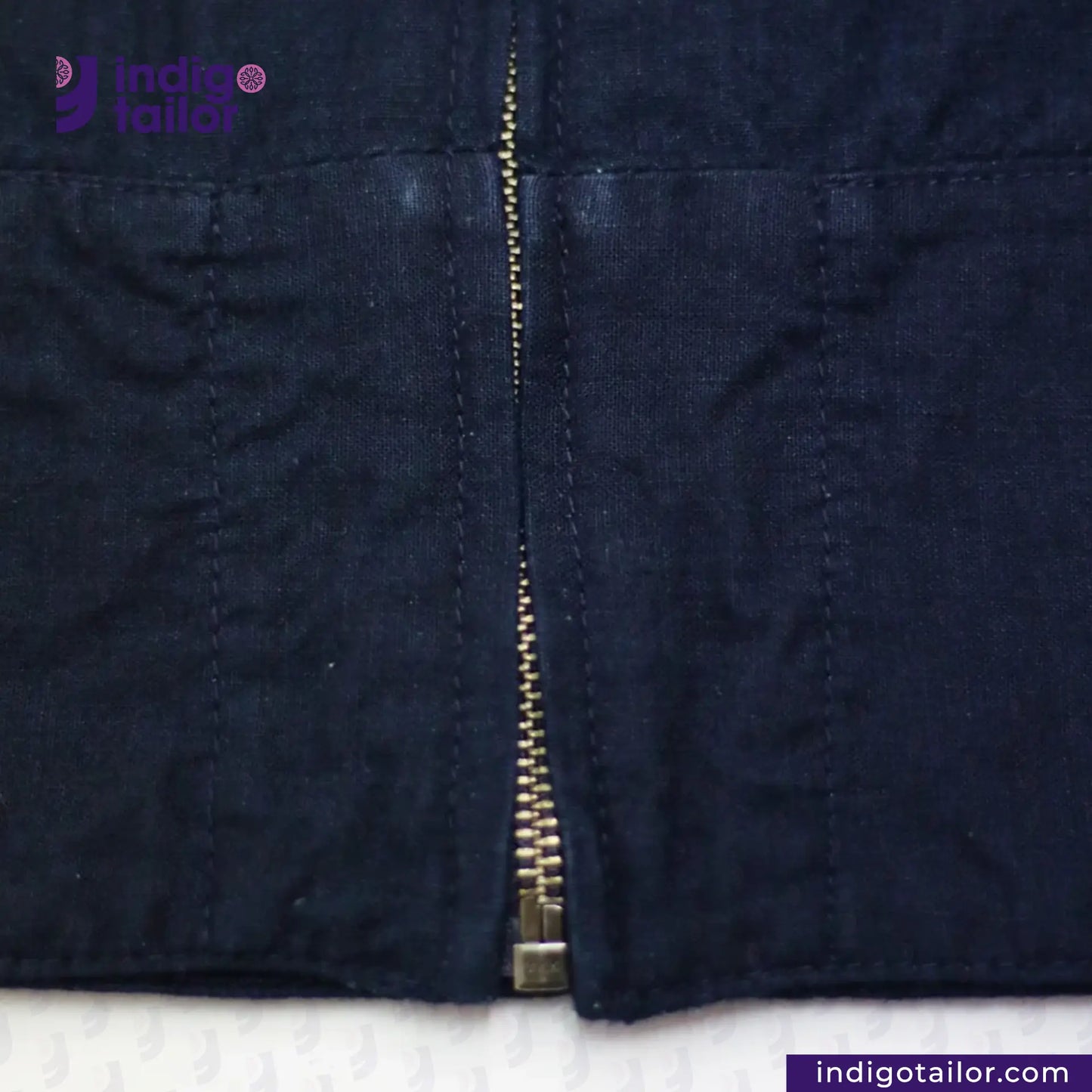 Close-up of a INDIGO HARRINGTON JACKET with a zipper on a white background, featuring the Indigo Tailor logo.