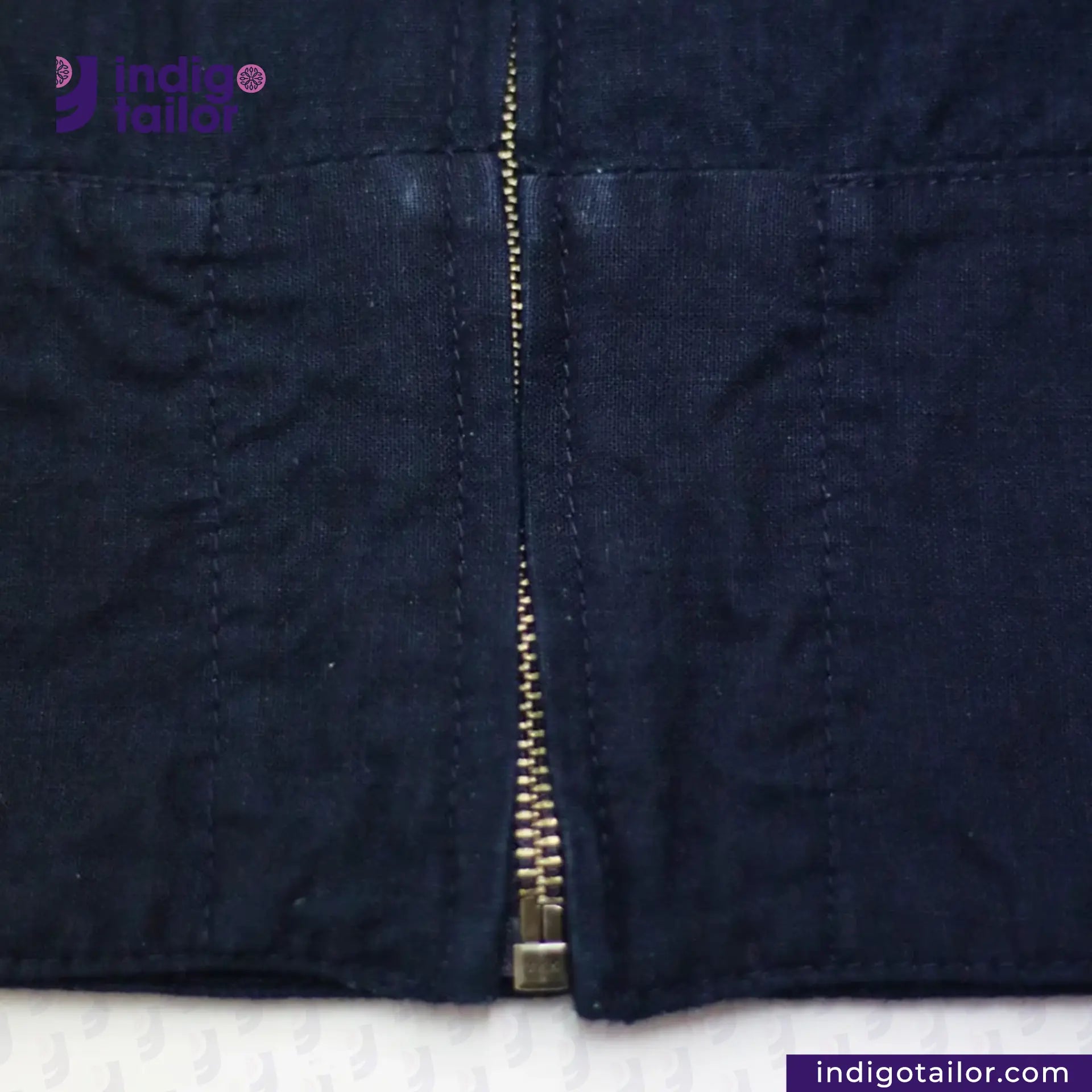Close-up of a INDIGO HARRINGTON JACKET with a zipper on a white background, featuring the Indigo Tailor logo.