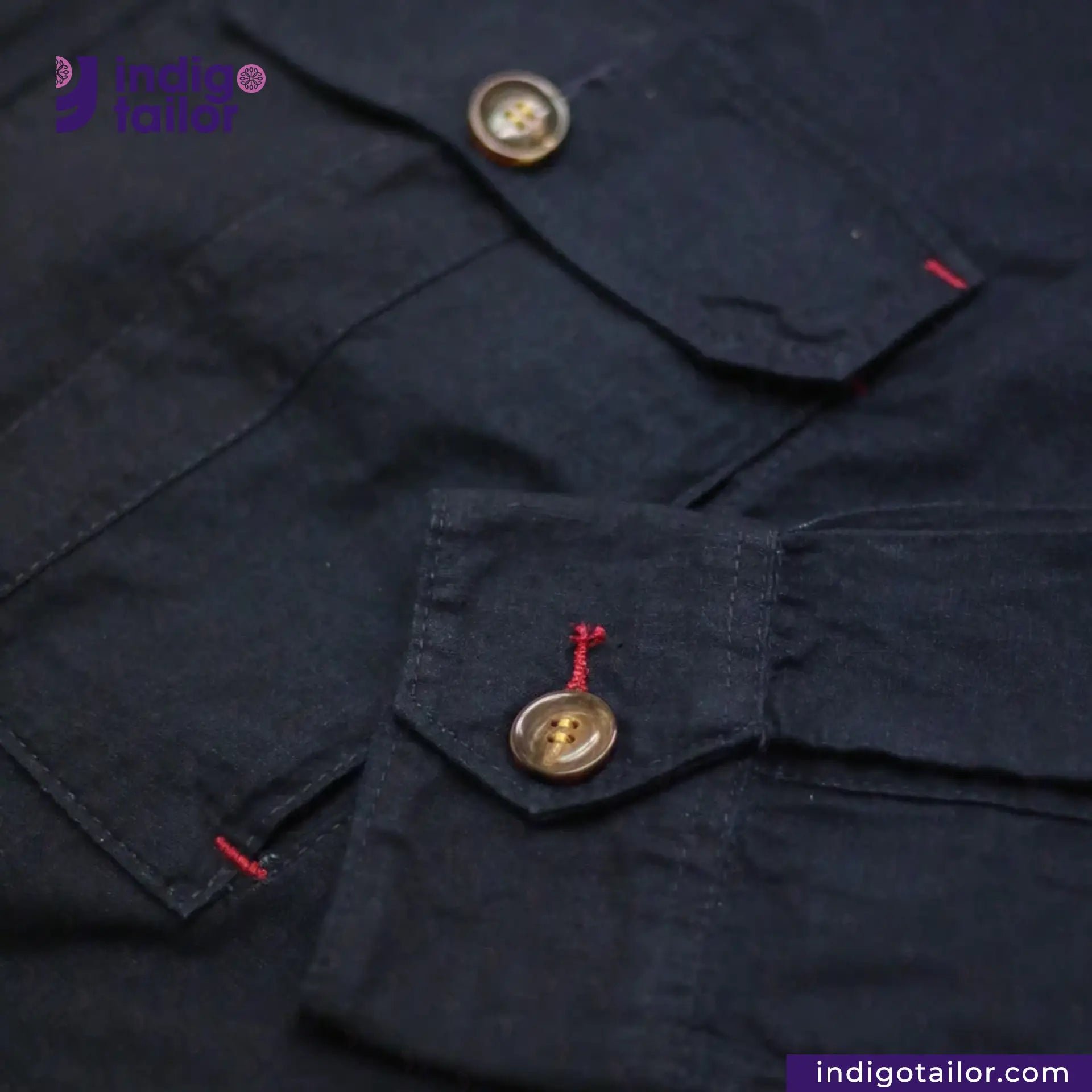 Close-up of a INDIGO HARRINGTON JACKET with buttons and red stitching, featuring 'Indigo Tailor' branding.