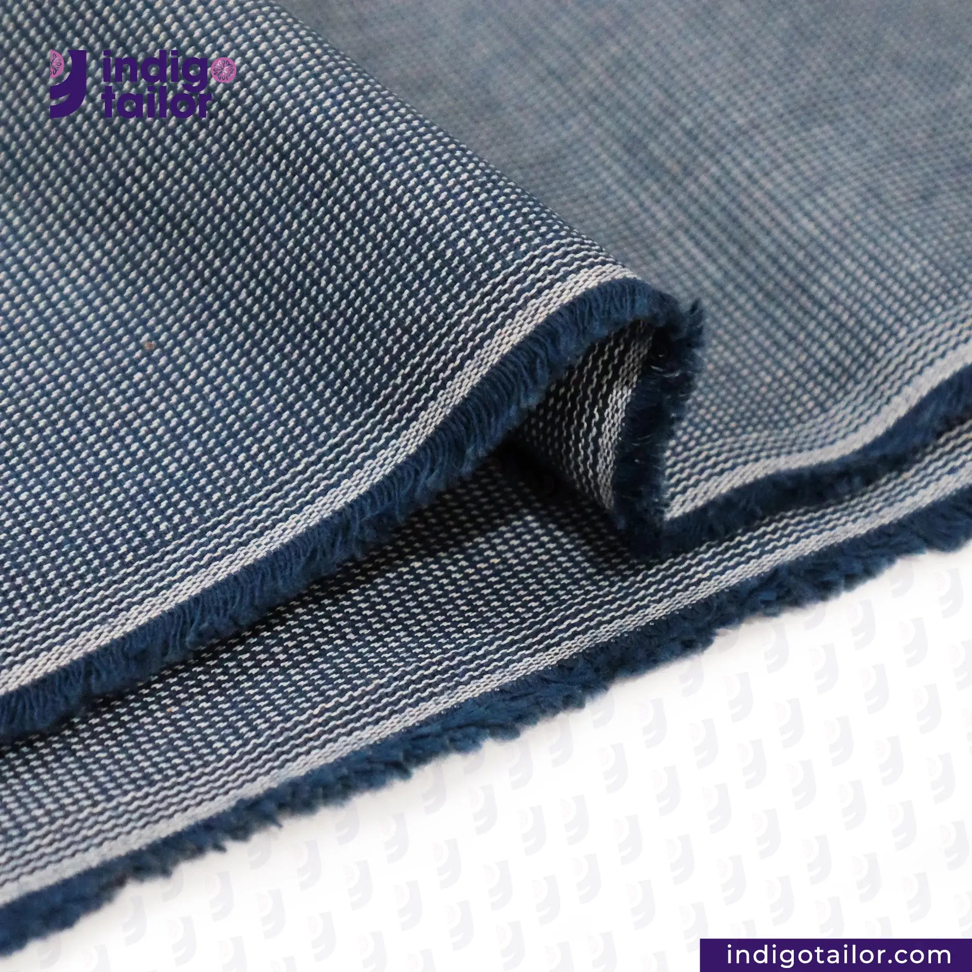 Close-up of INDIGO HOUNDSTOOTH denim fabric with 'Indigo Tailor' logo and website.