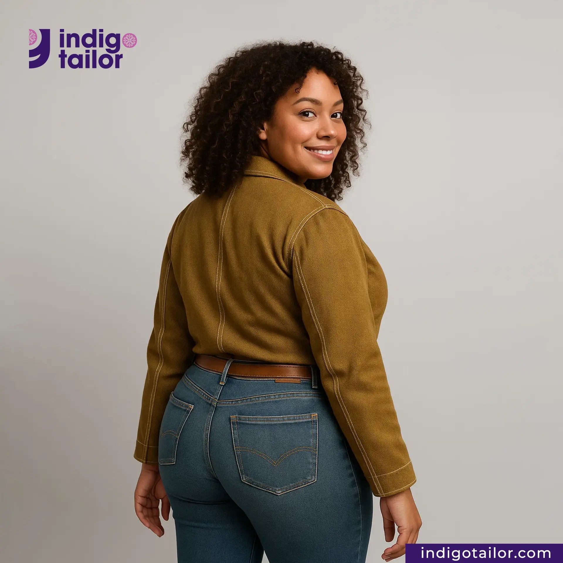 Woman wearing a KHAKI HERRINGBONE COVERALL JACKET jacket and blue jeans with 'Indigo Tailor' logo and website on a gray background