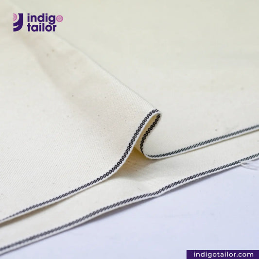 Close-up of KINARI SELVEDGE DENIM fabric with black stitching, featuring the Indigotailor logo.