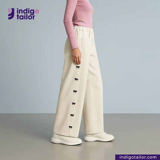 Person wearing KINARI SELVEDGE DENIM pants with black bow details and a pink top, standing against a gray background with 'indigotailor' branding.