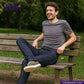 Man sitting on a bench wearing a gray t-shirt and NATURAL INDIGO DENIM jeans, with 'Indigo Tailor' branding.