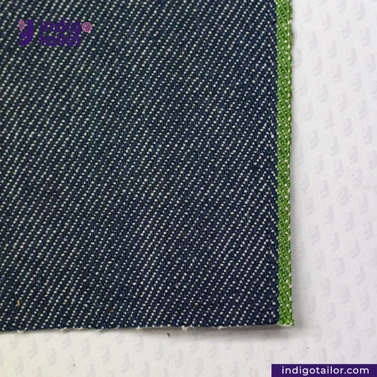 Close-up of OCEAN BLUE COTTON HEMP BLEND SELVEDGE DENIM fabric with a green edge on a white background, featuring the Indigo Tailor logo.