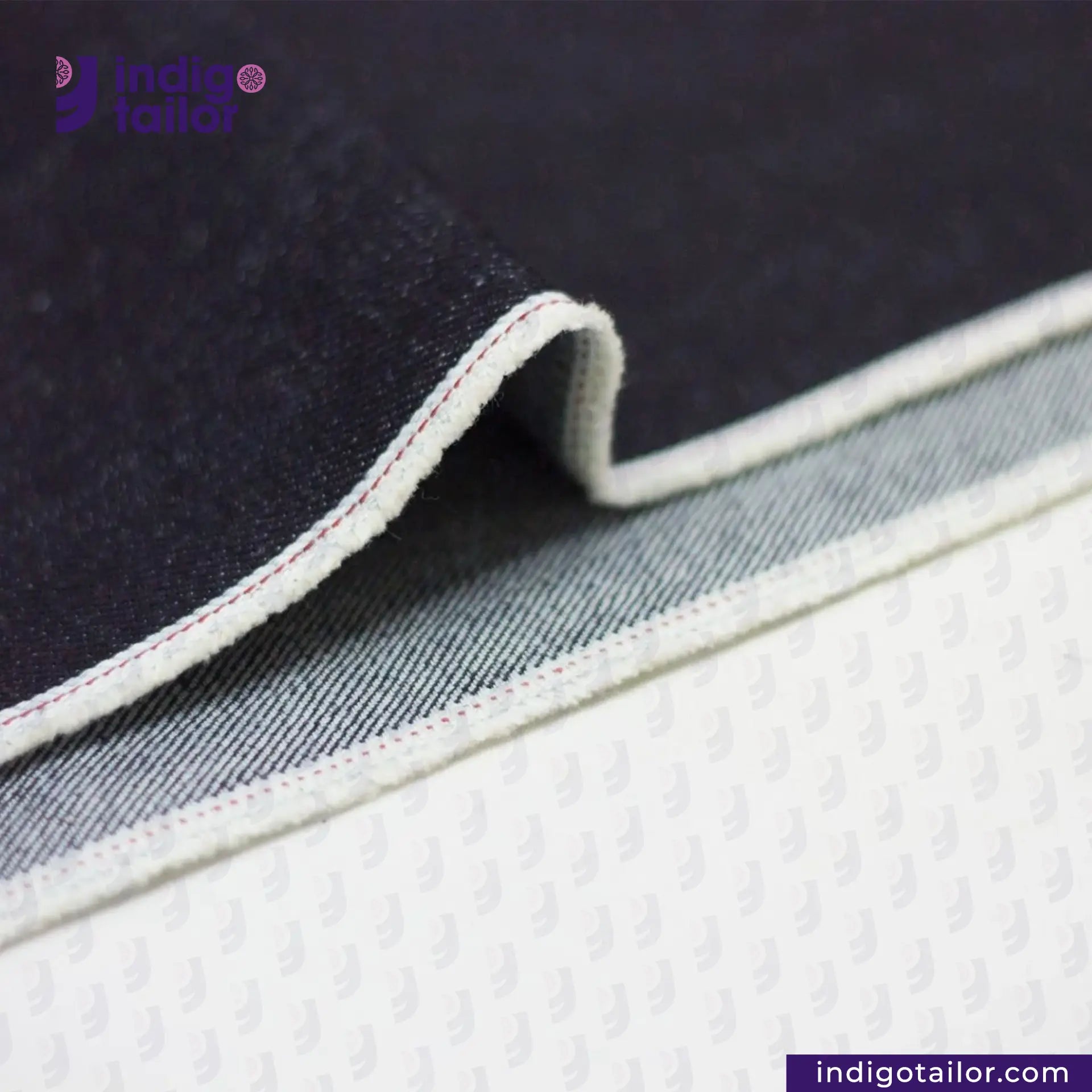 Close-up of ORIGINAL BLUE SELVEDGE DENIM fabric with visible stitching on a white background, featuring the Indigo Tailor logo.