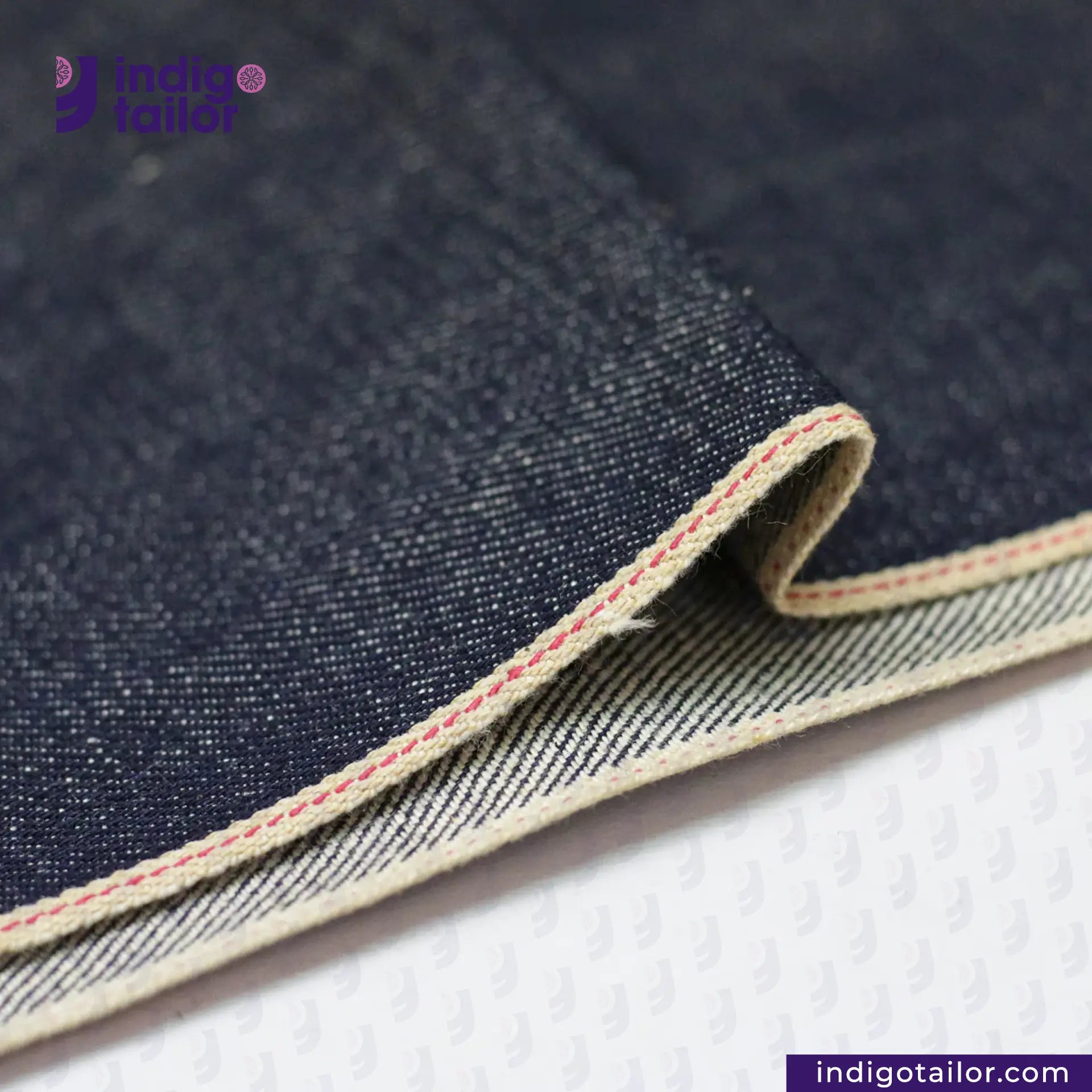 Close-up of RIGID INDIGO SELVEDGE DENIM fabric with visible stitching, featuring the Indigotailor logo.