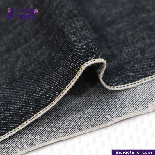 Close-up of ROUGH-SPUN DENIM FUZZY HANDFEEL fabric with visible stitching, featuring the Indigo Tailor logo.