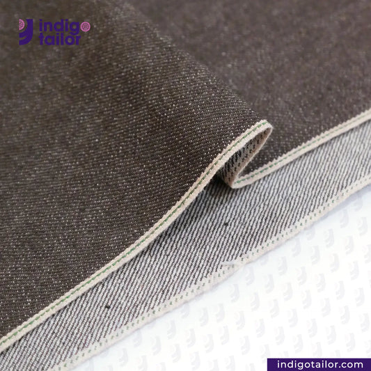 Close-up of SLUBBY BROWN SELVEDGE DENIM fabric with 'Indigo Tailor' logo and website URL.