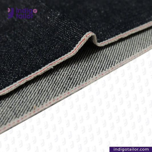 Close-up of SNOWY SELVEDGE DENIM fabric with visible stitching on a white background, featuring the Indigotailor logo.