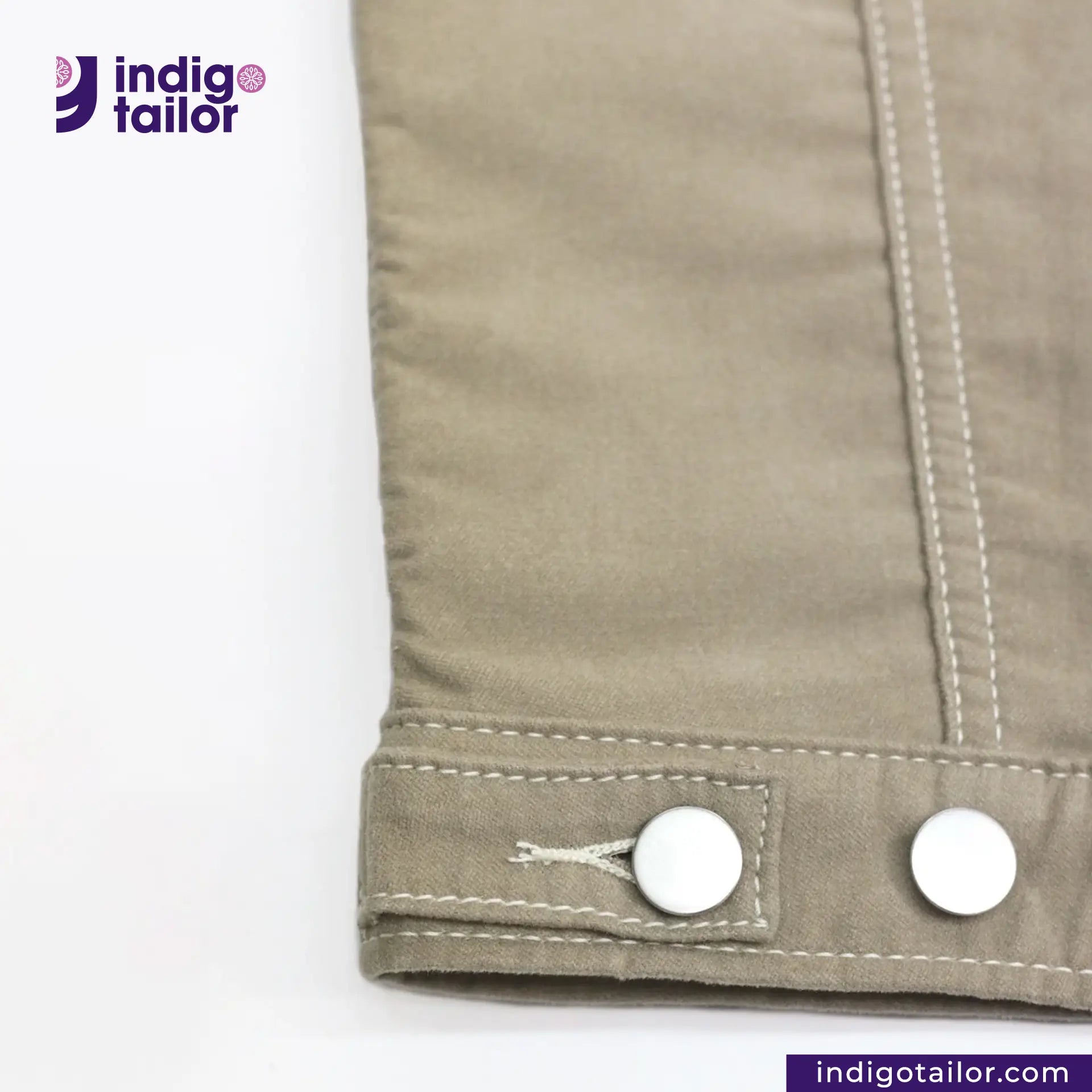 Close-up of a buttoned SUEDE JACKET cuff with 'Indigo Tailor' branding.