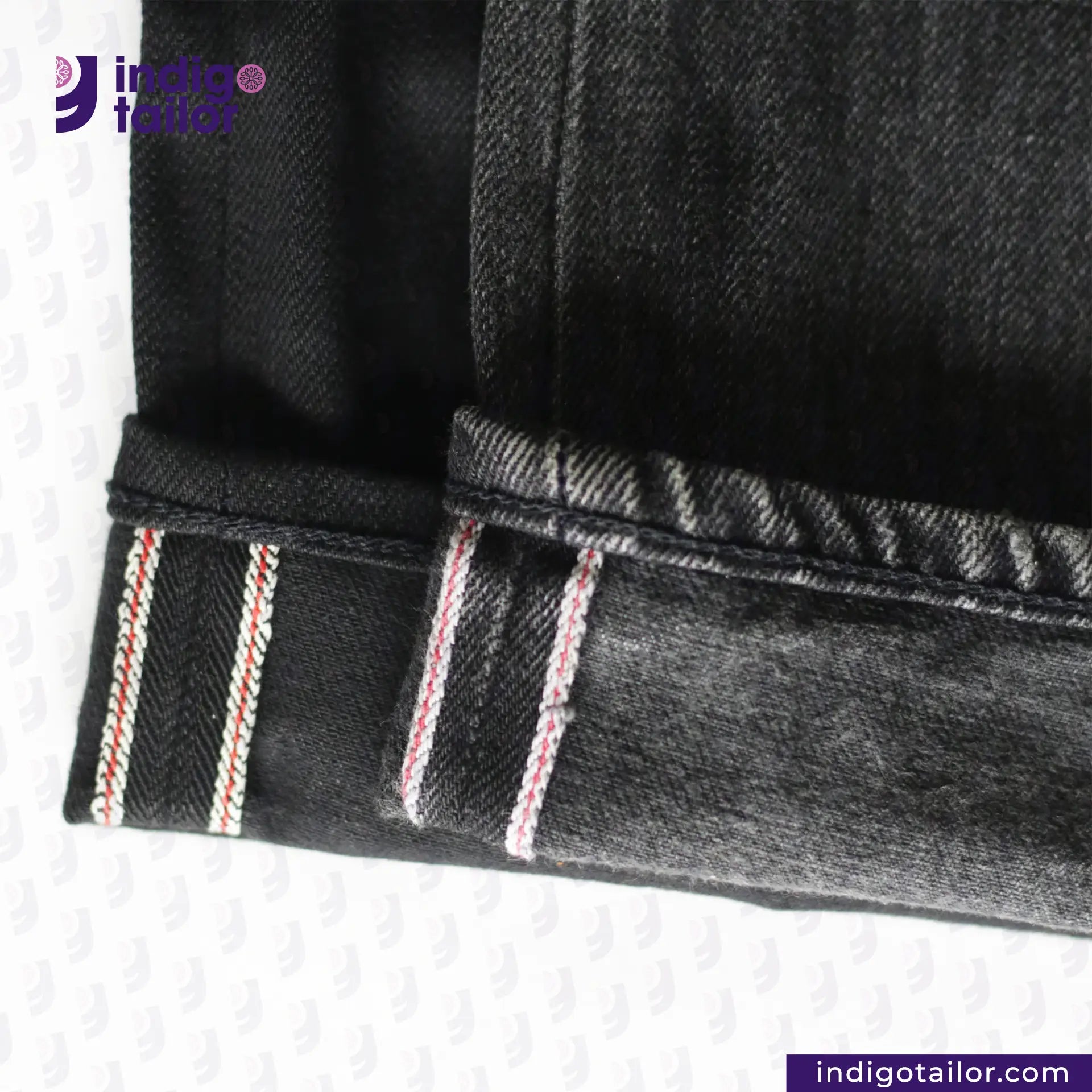 Close-up of SUPER BLACK DENIM jeans with red and white stitching on a white background, featuring the 'Indigo Tailor' brand.