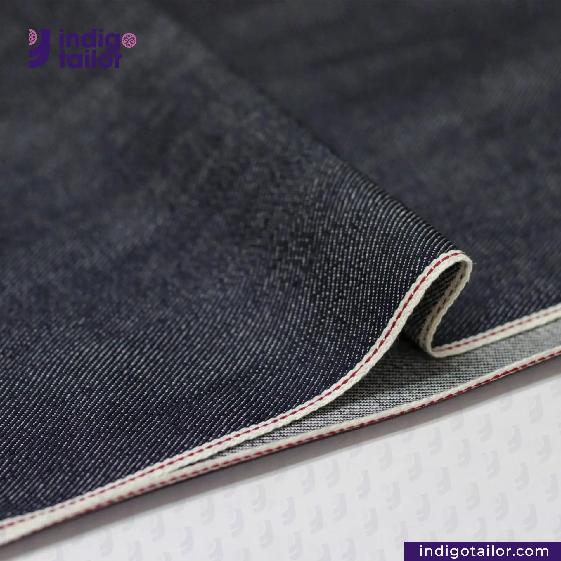Close-up of SUPER SOFT FLUFFY SELVEDGE DENIM fabric with visible stitching on a white background, featuring the Indigotailor logo.