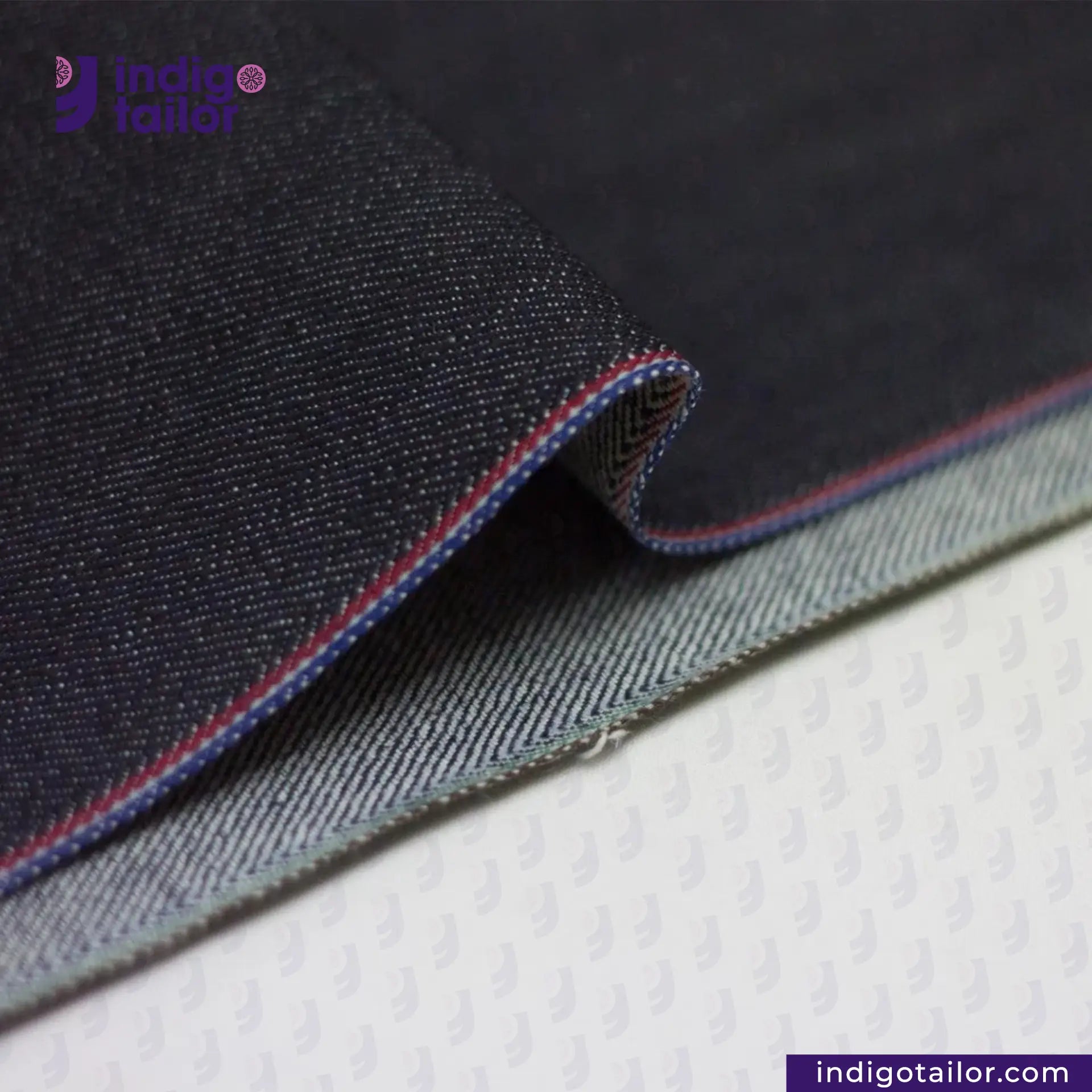 Close-up of TWO TONE STRETCH SELVEDGE DENIM fabric with red stitching on a white background, featuring the Indigotailor logo.
