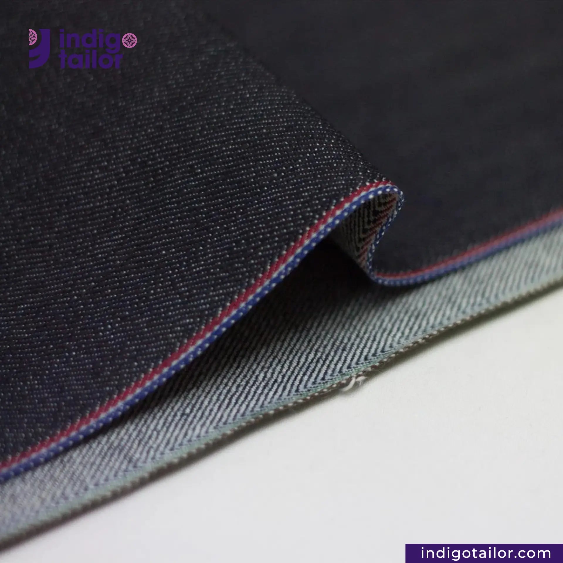 Close-up of TWO TONE STRETCH SELVEDGE DENIM fabric with visible stitching on a white background, featuring the Indigotailor logo.