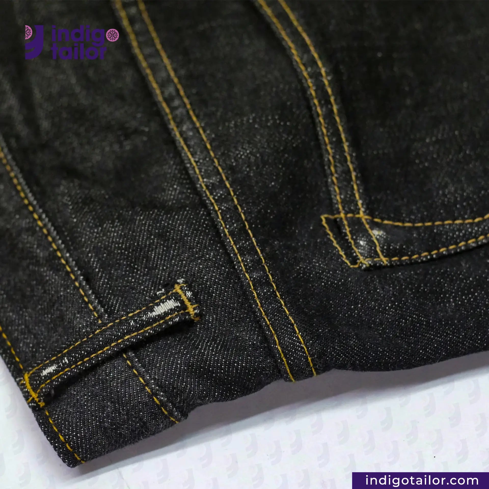 Close-up of VINTAGE CLASSIC BLACK DENIM fabric with yellow stitching on a white background, featuring the Indigotailor logo.