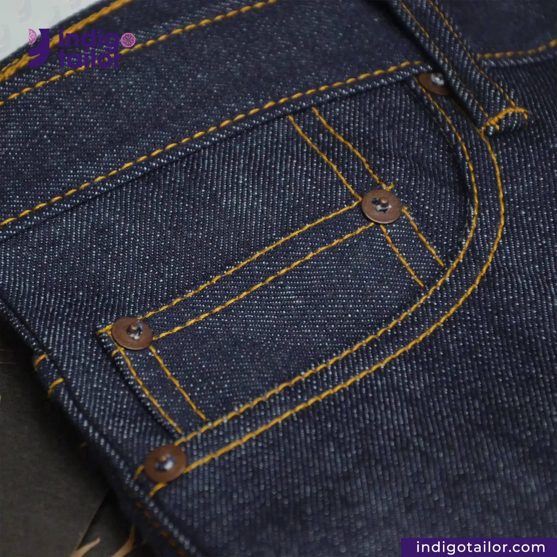 Close-up of VINTAGE SLUB DENIM jeans pocket area with yellow stitching, featuring 'Indigo Tailor' branding.