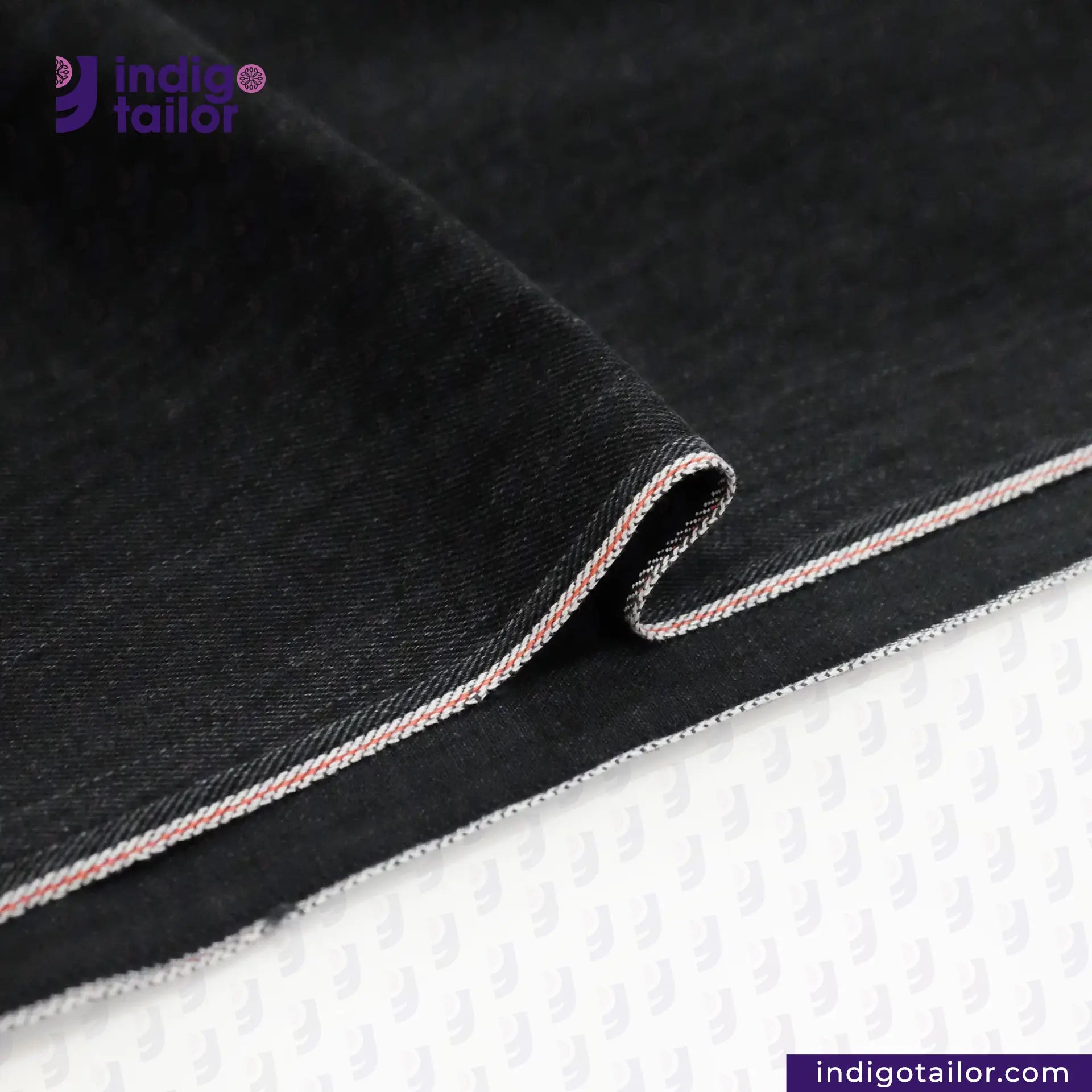 Close-up of WASHED BLACK x BLACK SELVEDGE denim fabric with white stitching on a white background, featuring the Indigotailor logo.