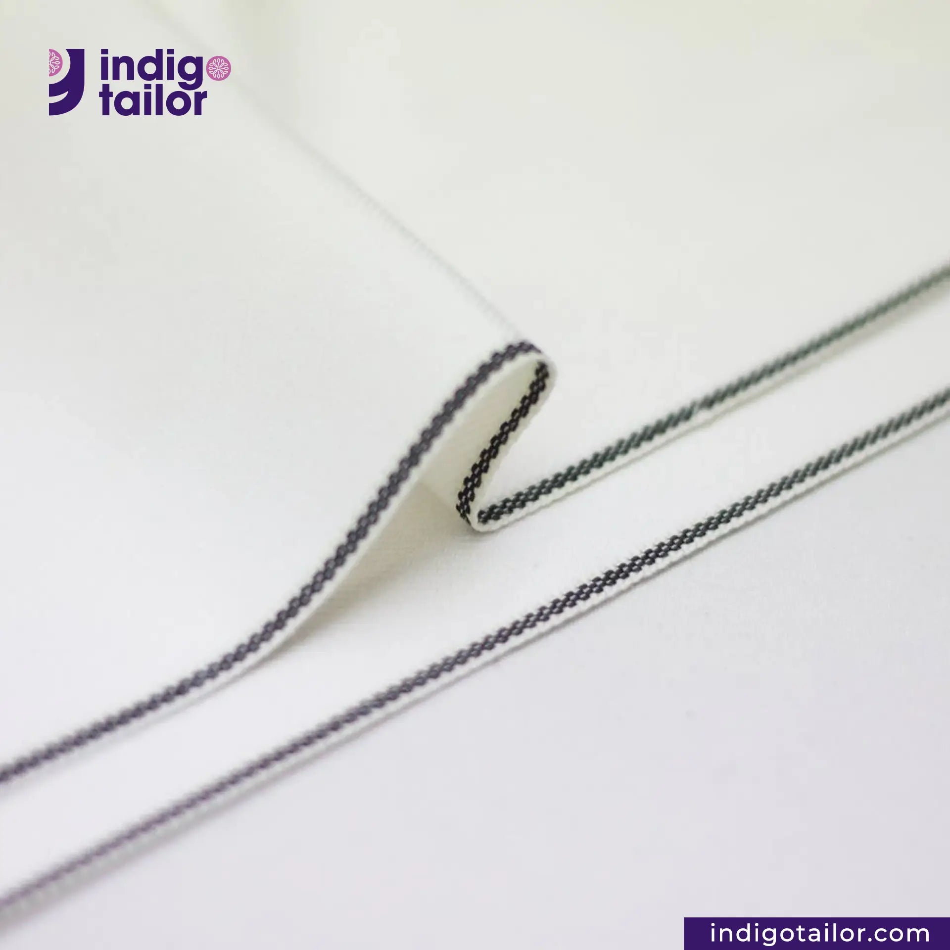 WHITE DENIM BLACK SELVEDGE, Close-up of a white fabric with black stitching, featuring the Indigotailor logo.